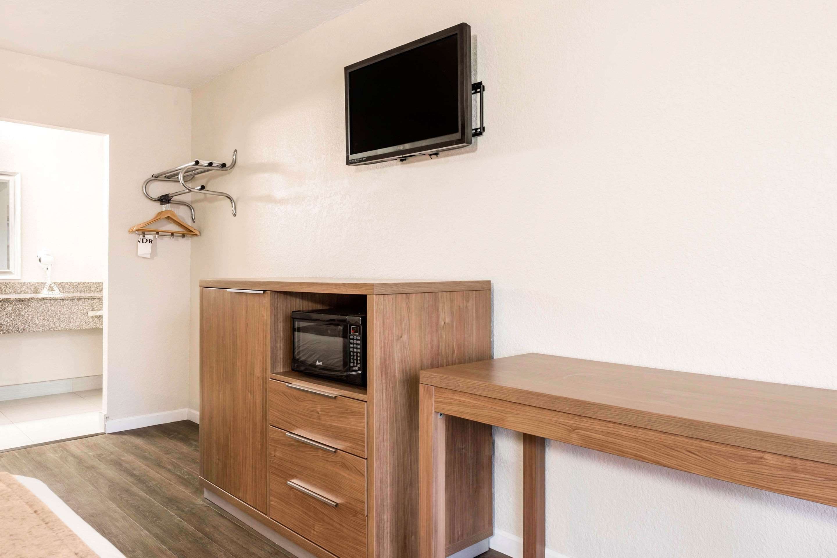 Una kitchenette con microondas, armarios de madera y un televisor montado en la pared.