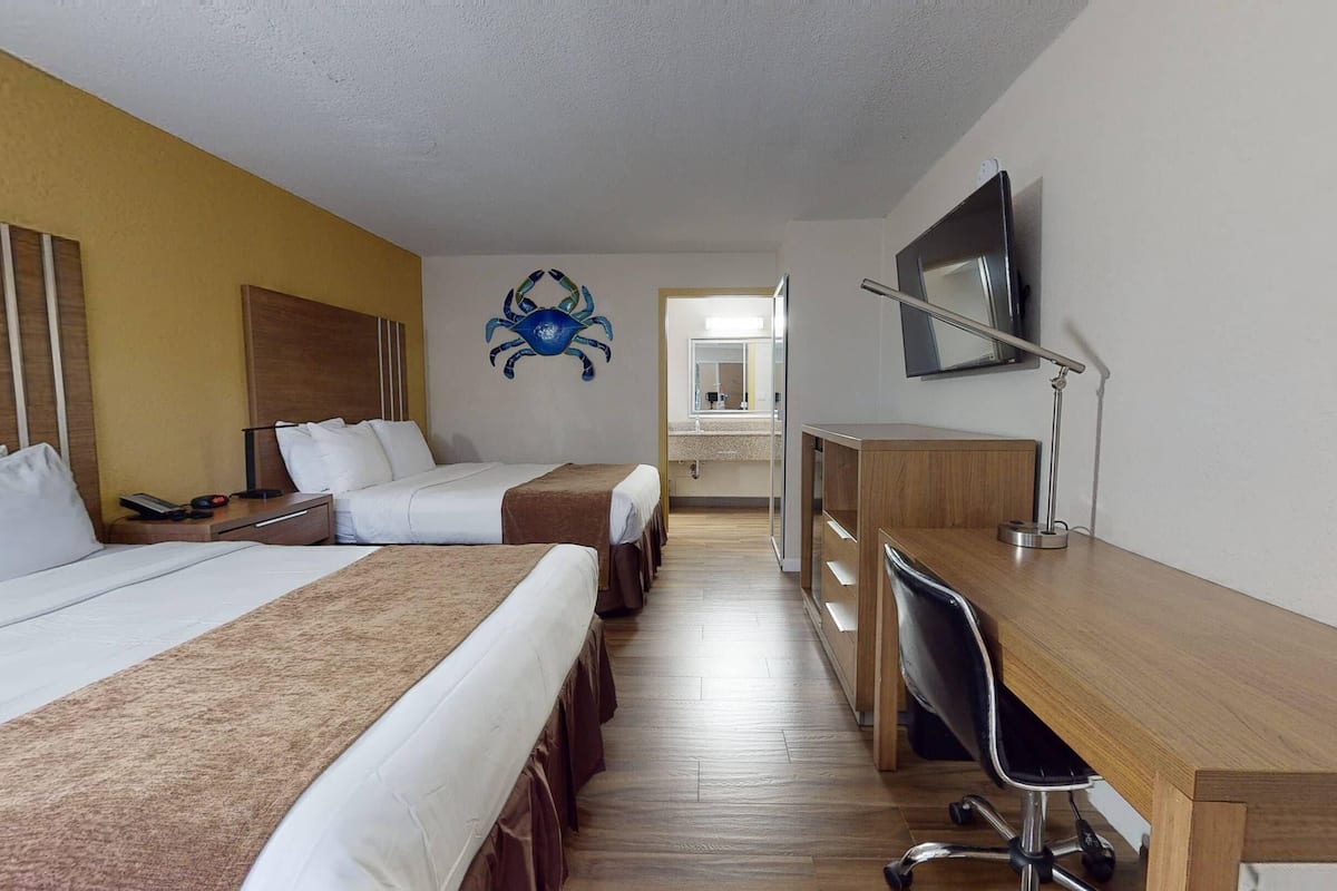 Een hotelkamer met twee bedden, een bureau, een televisie en een zichtbare badkamer op de achtergrond.