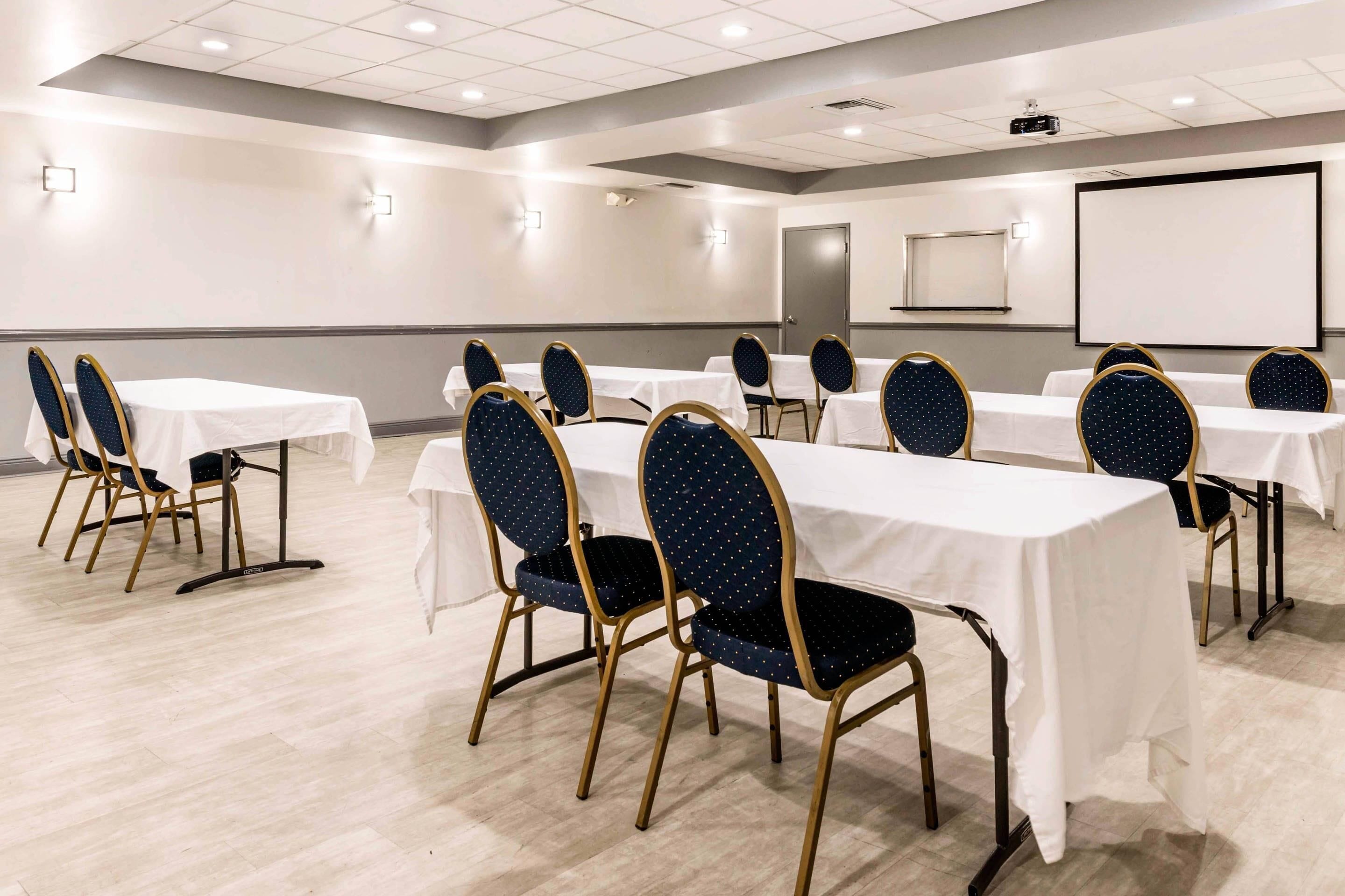 A conference room with tables and chairs, a projector screen, and a whiteboard.