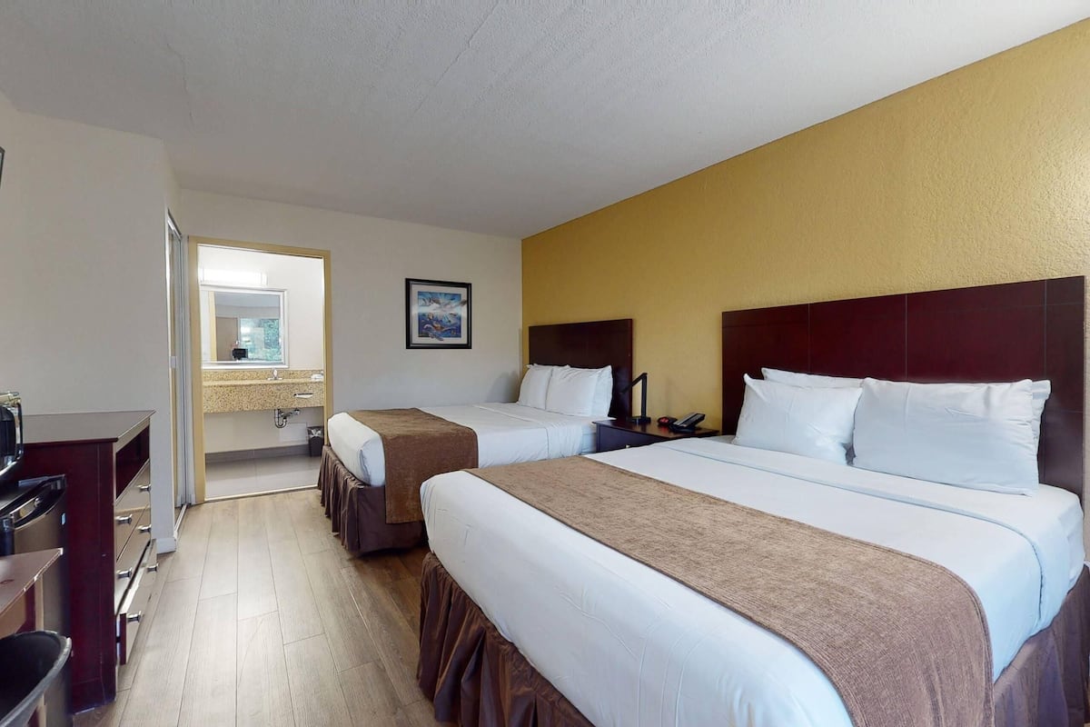 Een hotelkamer met twee bedden, een bureau en een badkamer, zichtbaar door een geopende deur.