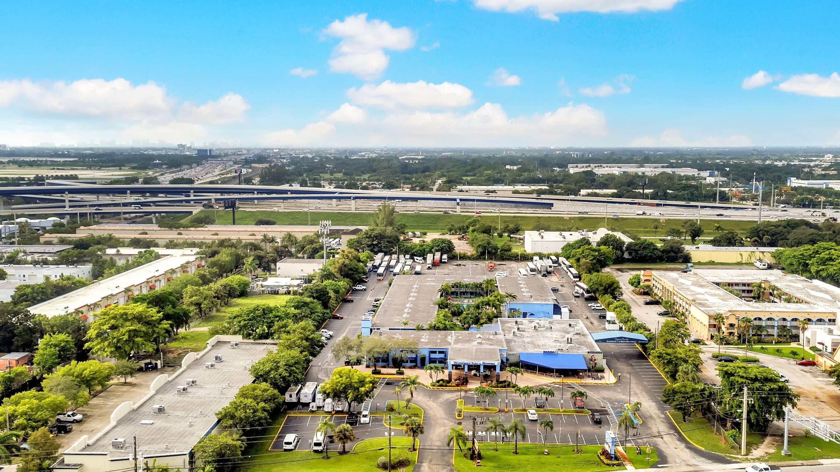 An airport terminal with multiple parking lots, green spaces, and a large building with a blue roof.