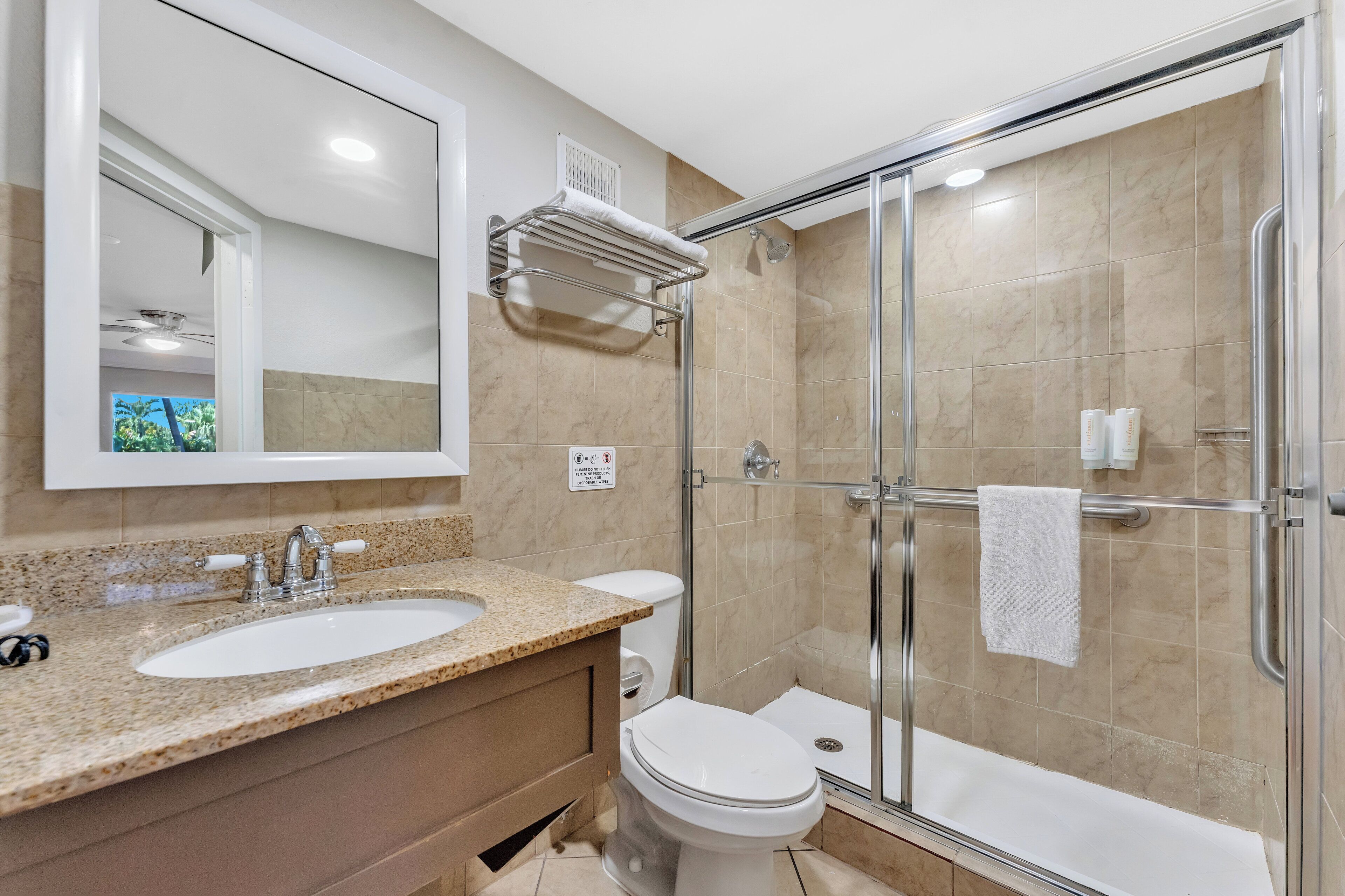 A modern bathroom with a granite countertop sink, a toilet, and a glass-enclosed shower.