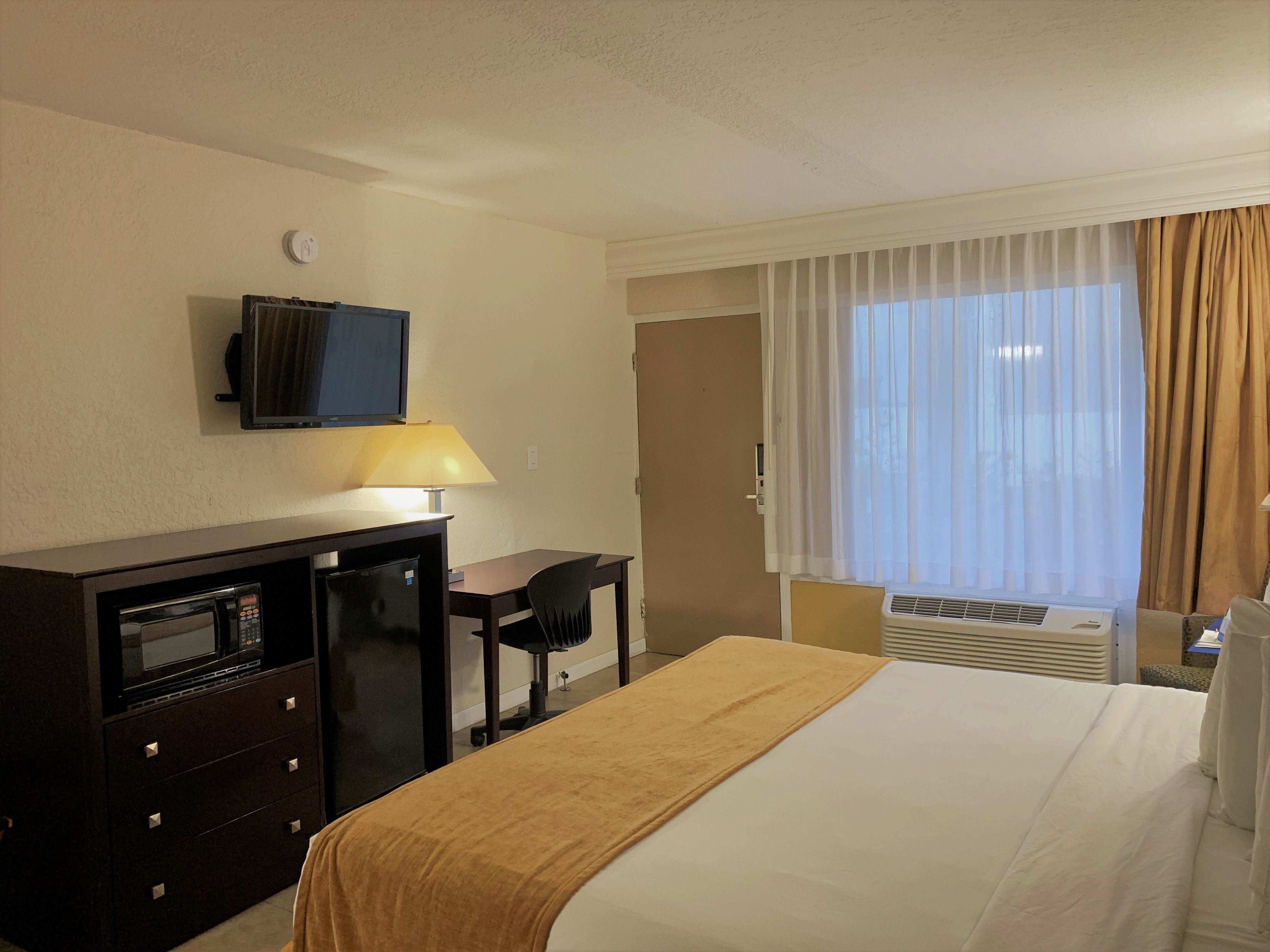 Ein Hotelzimmer mit Bett, Schreibtisch mit Computer, Fernseher und einem Fenster mit Vorhängen.
