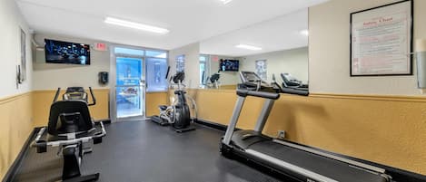 A gym with treadmills, an elliptical, and a stationary bike. There is a safety chart on the wall and an exit sign.