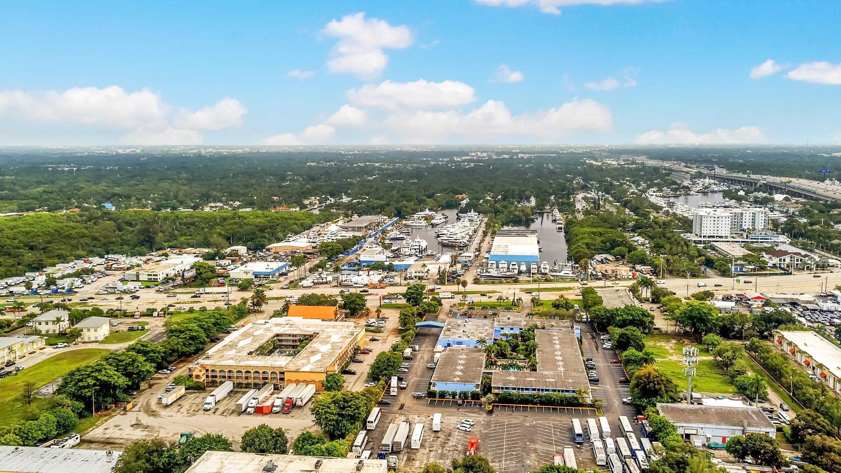 An aerial view of a city with a marina, industrial buildings, and a large parking area.