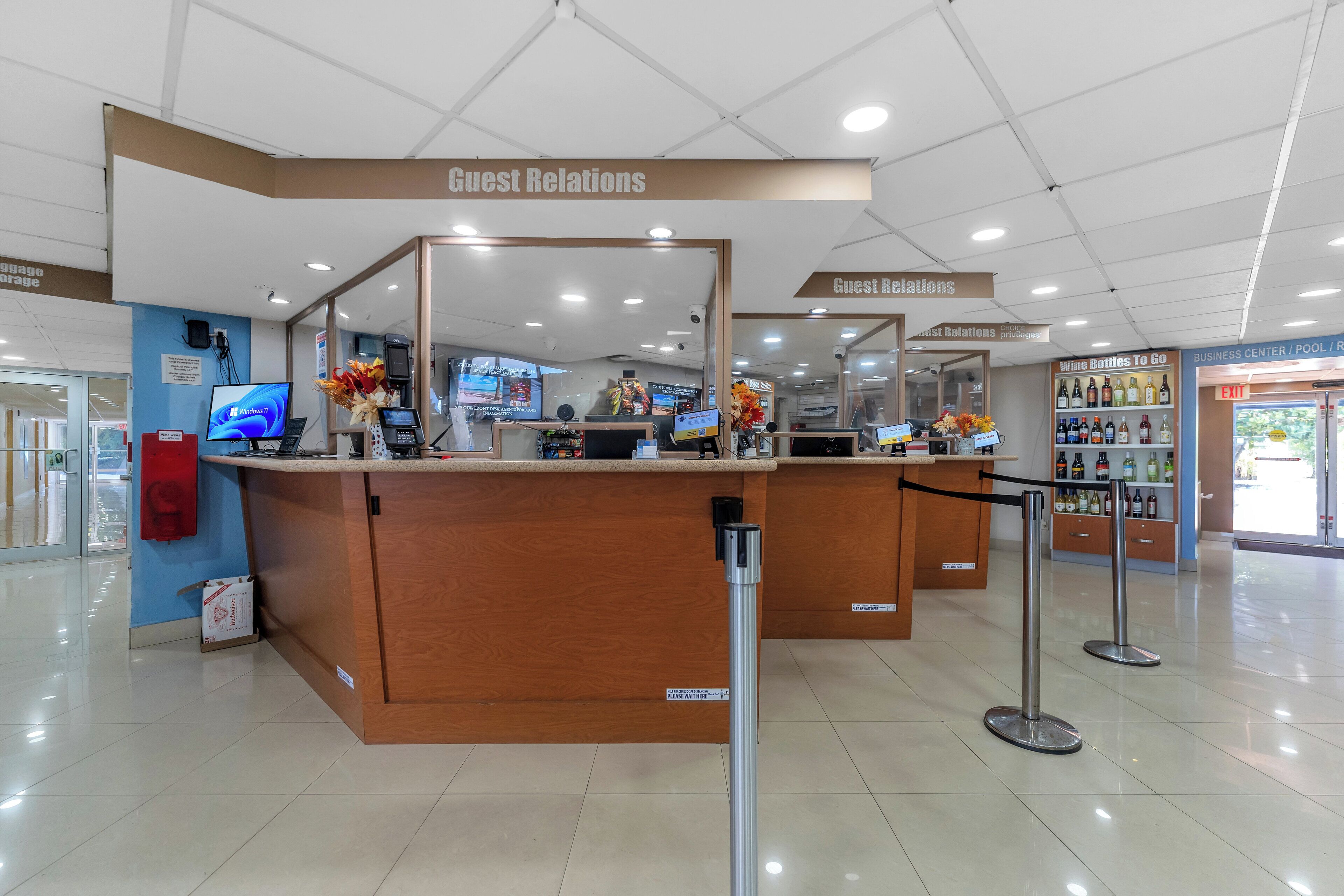 A hotel reception area with a 'Guest Relations' desk, a computer monitor, and a 'Wine Bottles To Go' section.