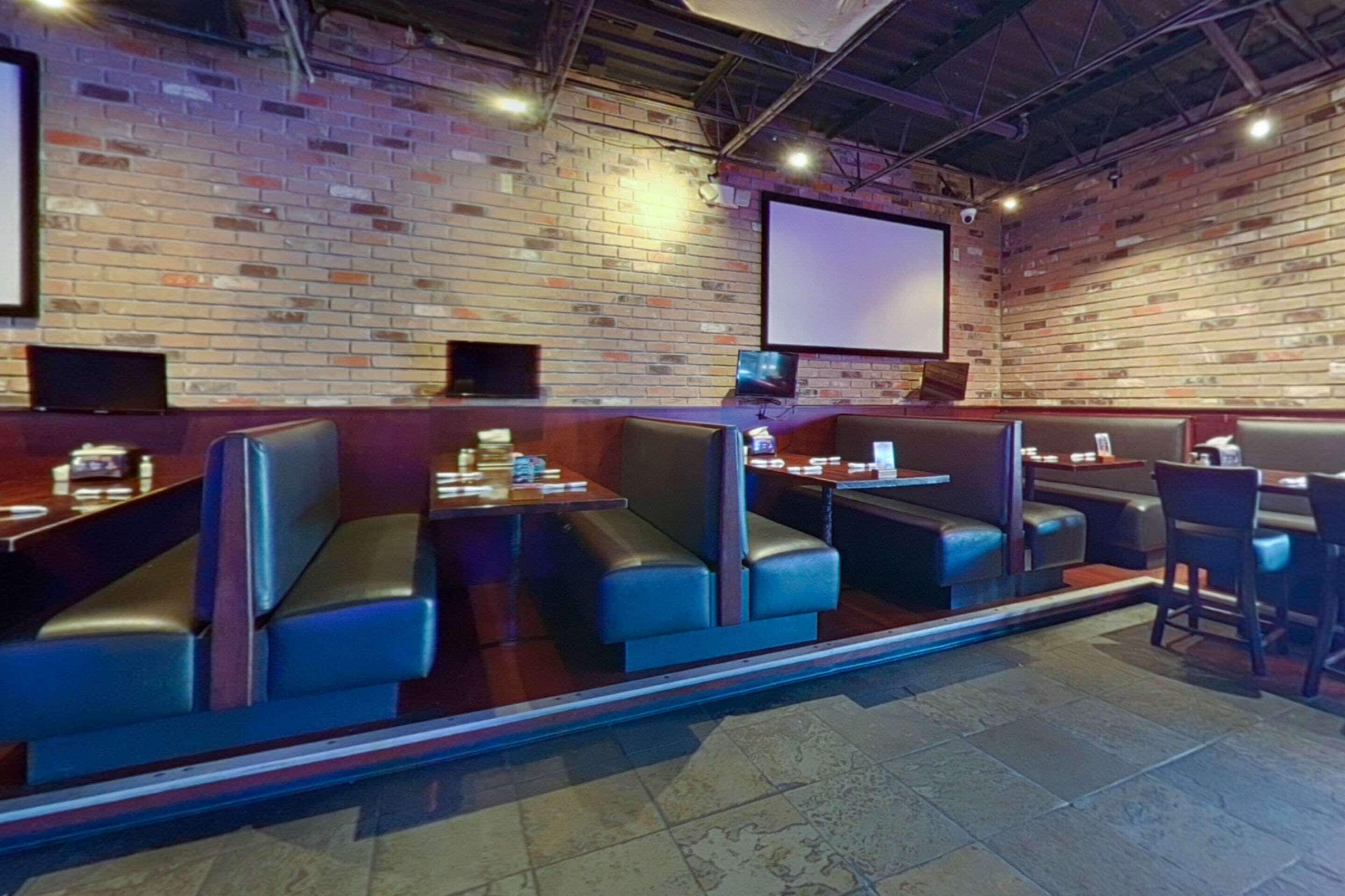 Un restaurant avec des banquettes et des tables, des murs en briques et un grand écran.