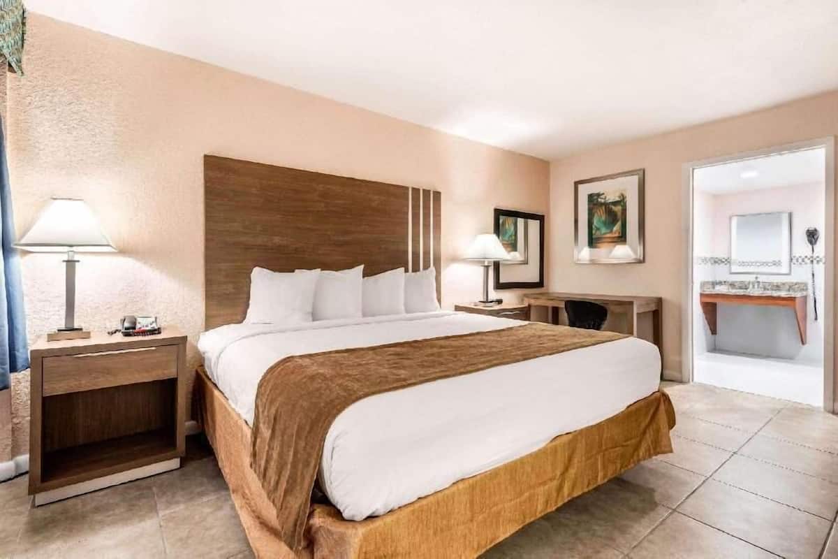 Hotelkamer met een groot bed, nachtkastjes, een bureau, een stoel, een spiegel en een badkamer zichtbaar door een open deur.