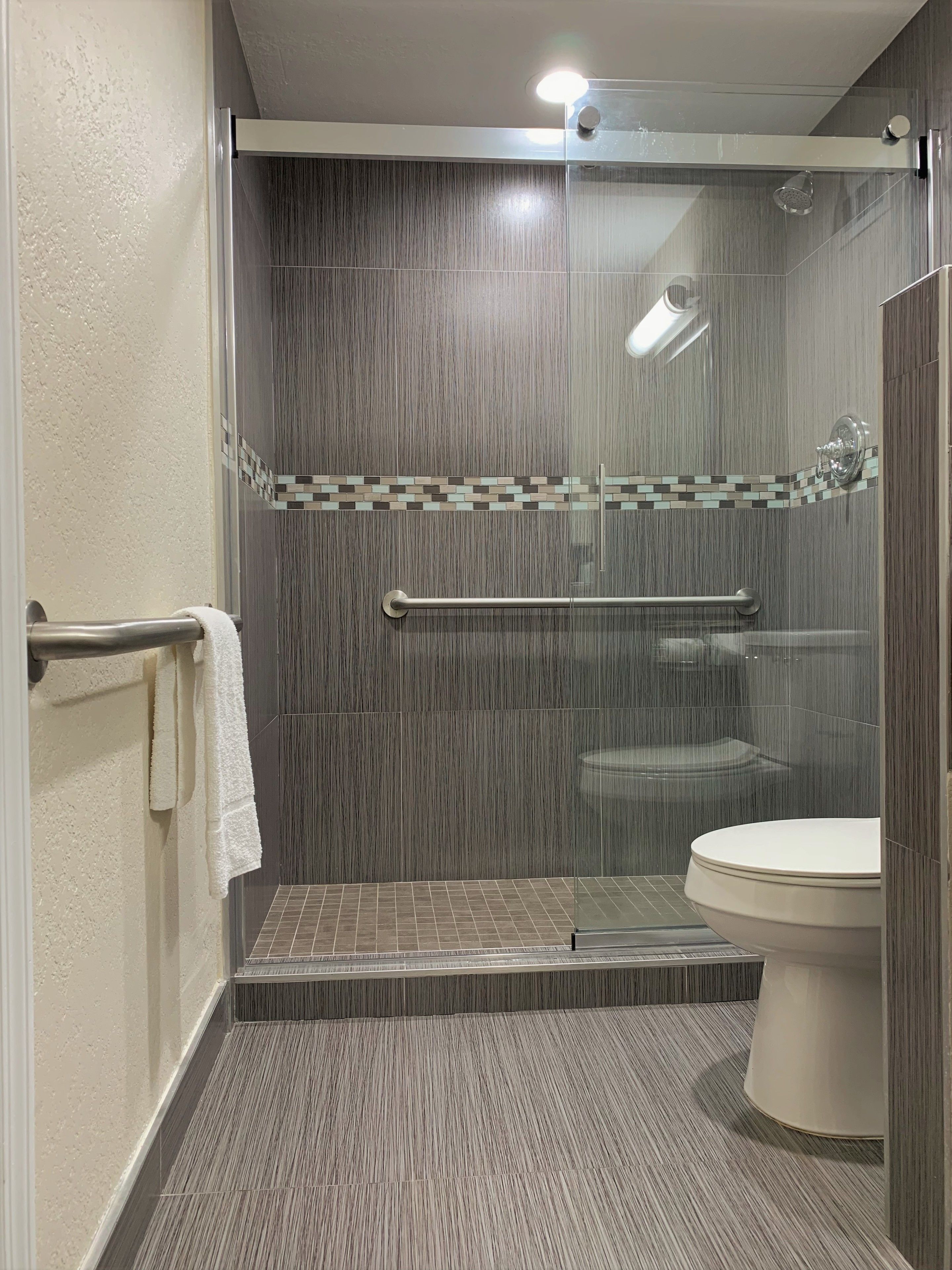 Un baño moderno con ducha de vidrio, inodoro blanco y piso de baldosas.
