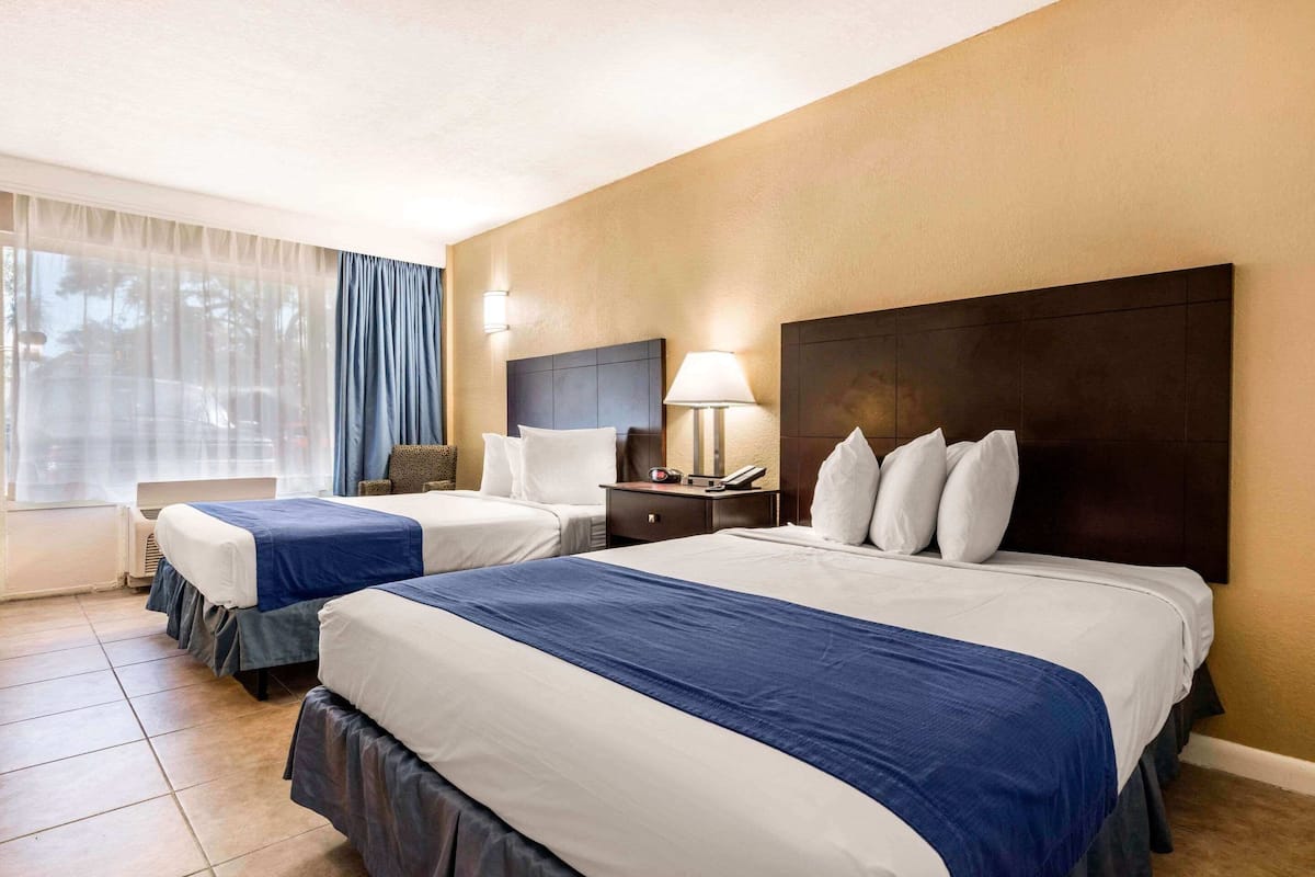 Een hotelkamer met twee bedden, een bureau, een stoel, een lamp en een raam met gordijnen.