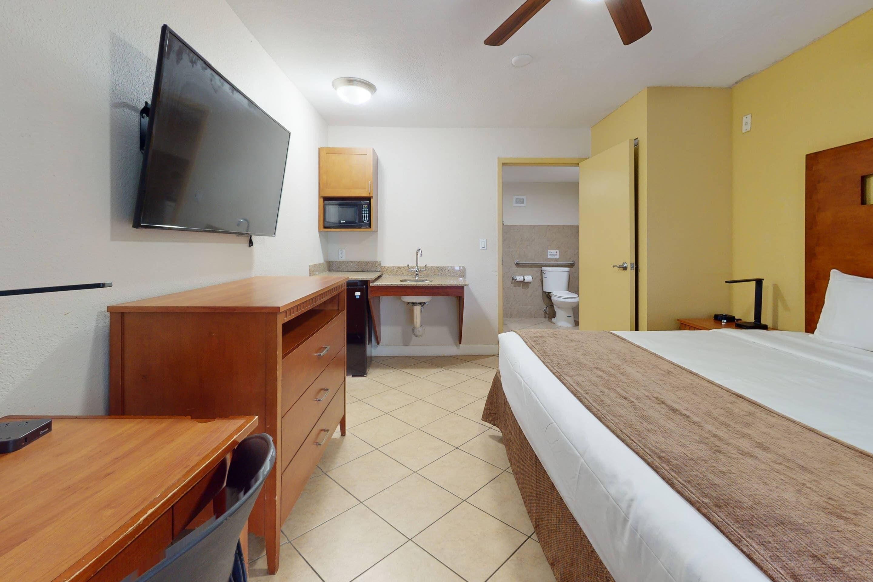 A hotel room with a bed, desk, chair, television, microwave, sink, and toilet.