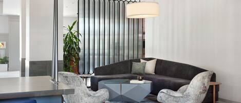 A modern living room with a dark grey sofa, two armchairs, a glass coffee table, and a large lamp.
