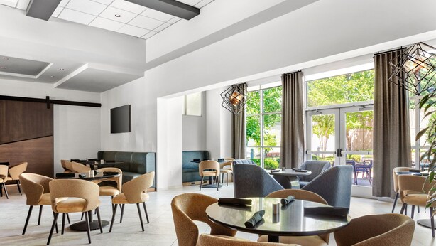 A modern hotel lobby with a central seating area, large windows, and a flat-screen TV mounted on the wall. - Delta Hotels by Marriott Midwest City at the Reed Conference Center (Midwest City)