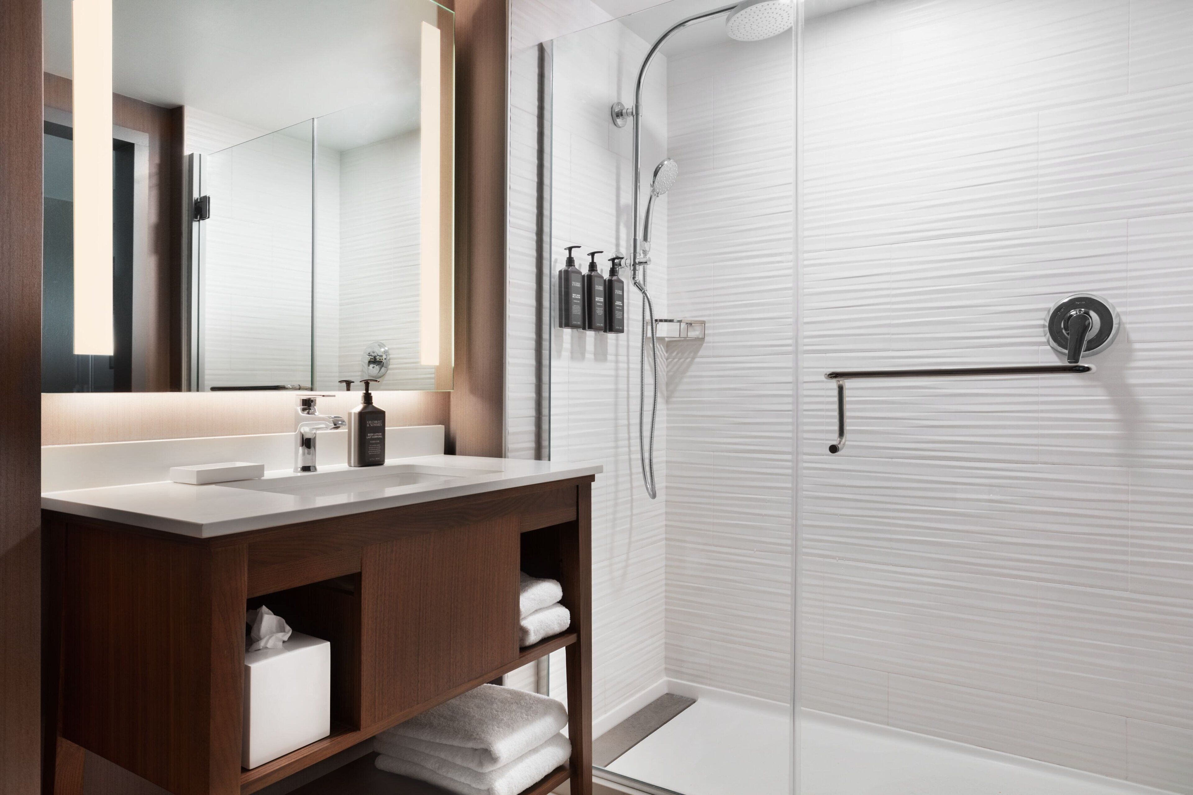 A modern bathroom with a wooden vanity, a large mirror, a shower with a glass door, and a towel rack.