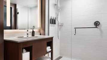 A modern bathroom with a wooden vanity, a large mirror, a shower with a glass door, and a towel rack.