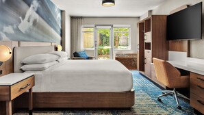 A hotel room with a bed, a desk, a chair, a TV, and a large window with a view of greenery. - Delta Hotels by Marriott Midwest City at the Reed Conference Center (Midwest City)