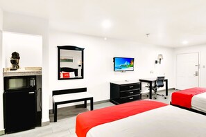 A hotel room with a bed, a desk, a chair, a TV, a microwave, and a bench.