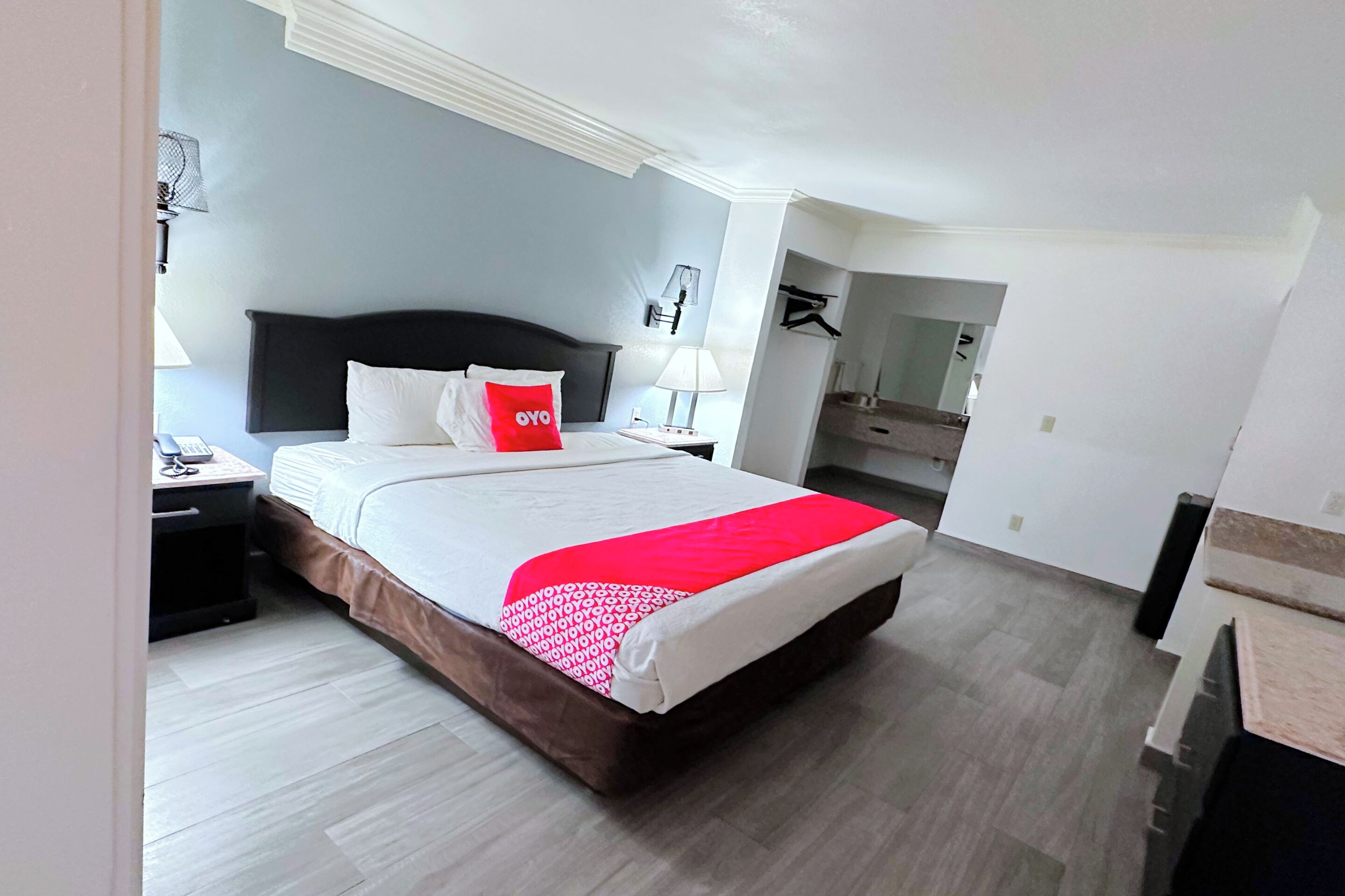 Quarto de hotel com uma cama grande, mesa de cabeceira, abajur e espelho.