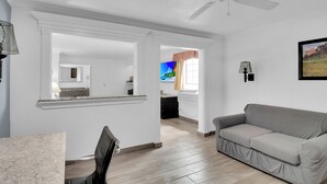 Ein geräumiges Wohnzimmer mit grauem Sofa, einem Essbereich mit Marmortisch und einer Küche im Hintergrund.