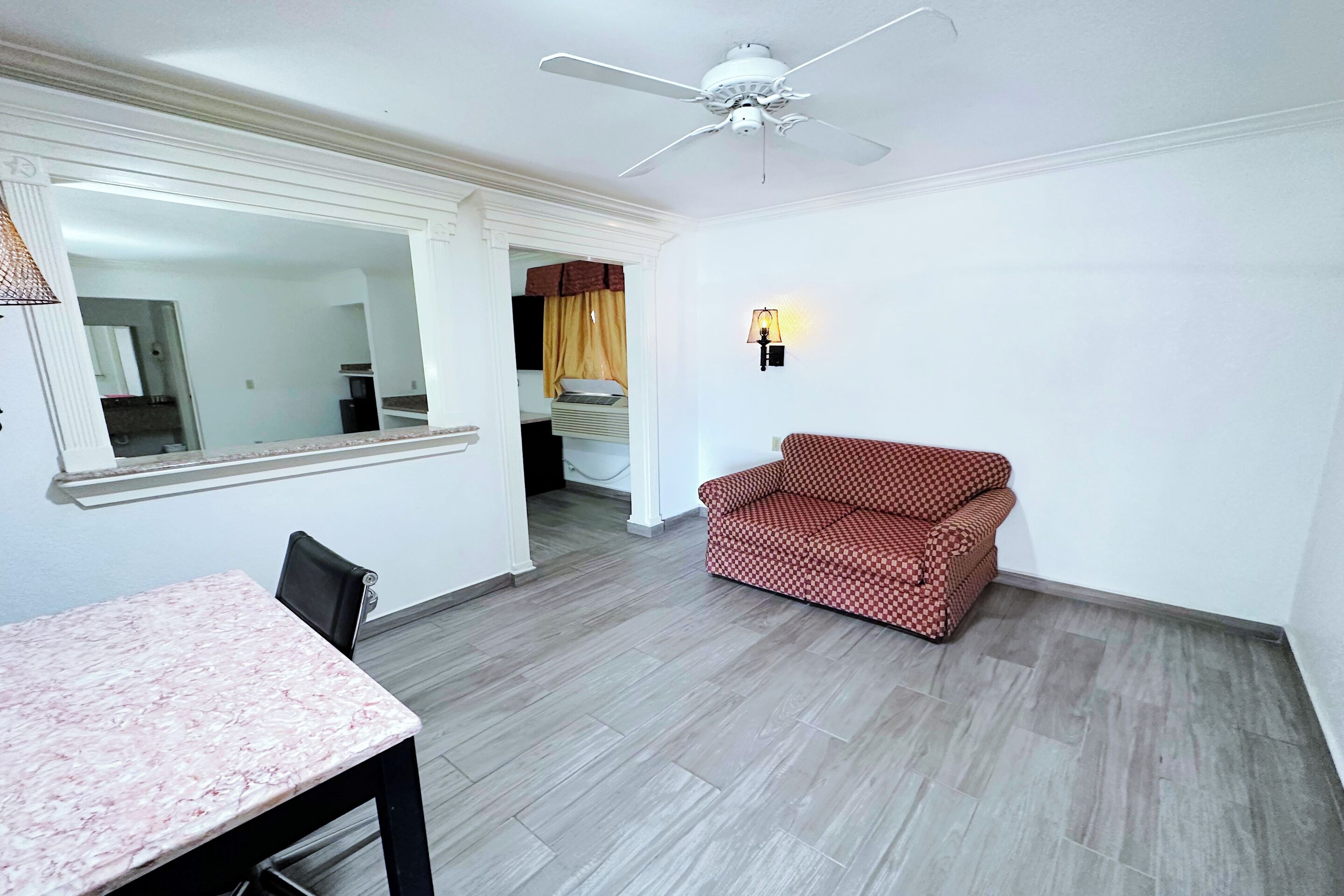 A room with a dining table, a red patterned sofa, a ceiling fan, and a wall-mounted lamp.