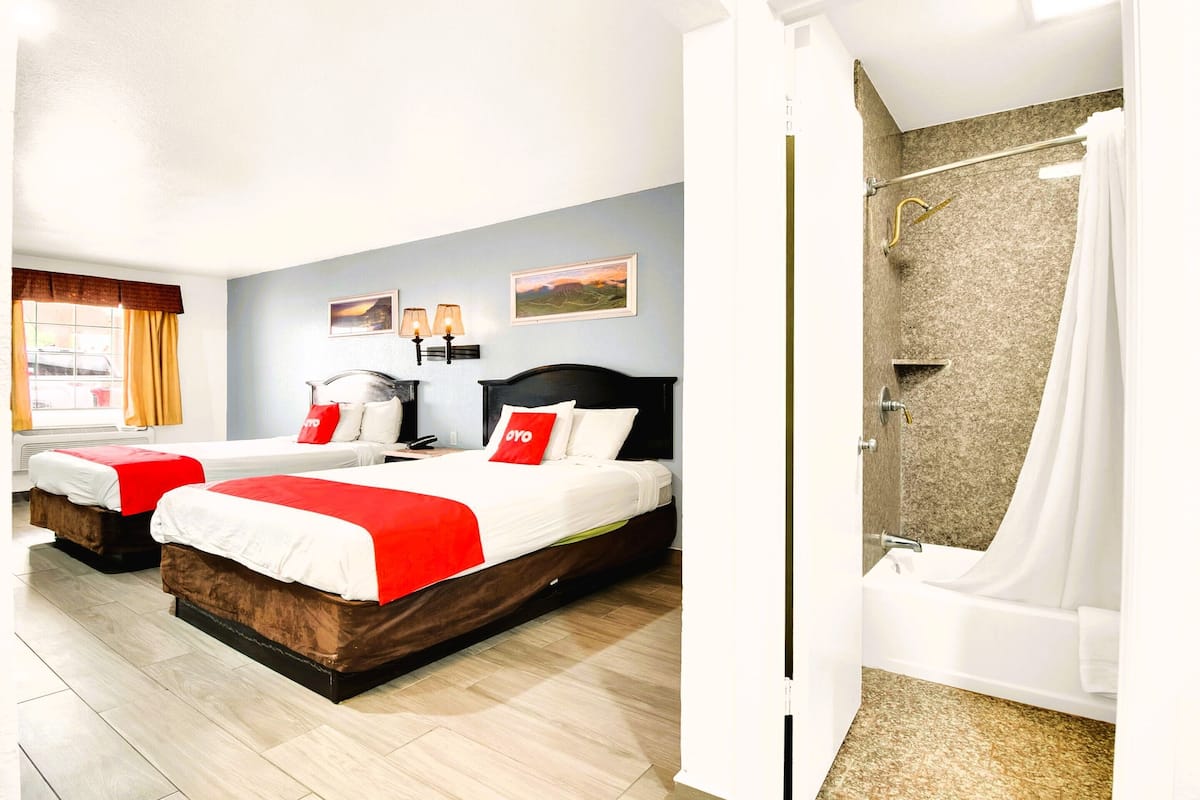 A hotel room with two beds, a shower, and a window with curtains.