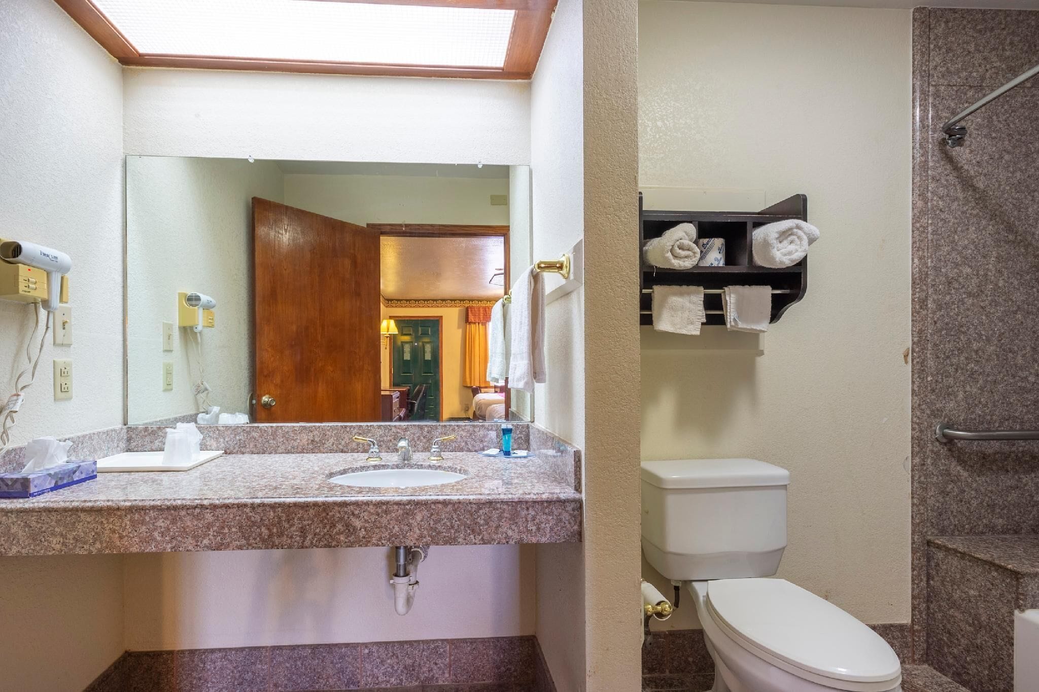 A bathroom with a granite countertop sink, a mirror, a towel rack, and a shower area.