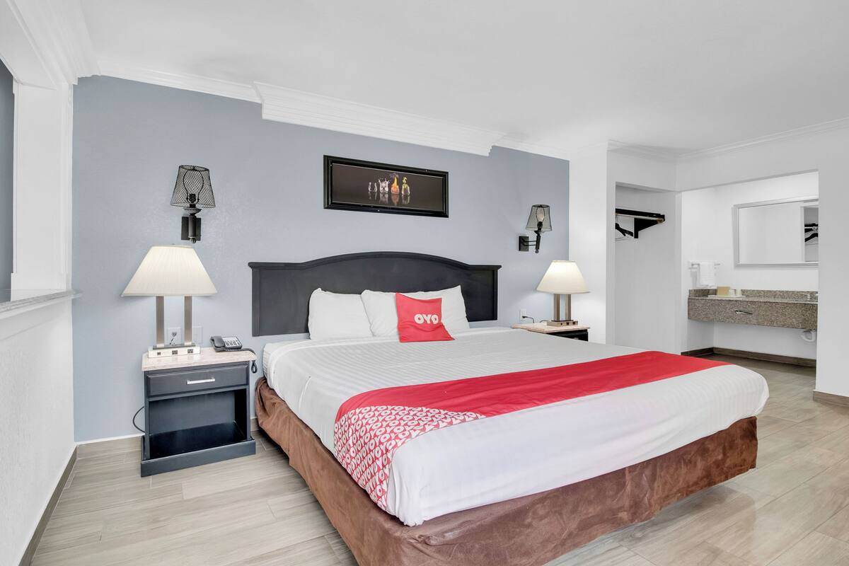 A hotel room with a large bed, two bedside tables, a nightstand, a mirror, and a wall-mounted artwork.