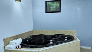 Ein Badezimmer mit einer großen schwarzen Badewanne, einem gerahmten Bild an der Wand sowie Handtüchern und Pflegeprodukten an der Seite.