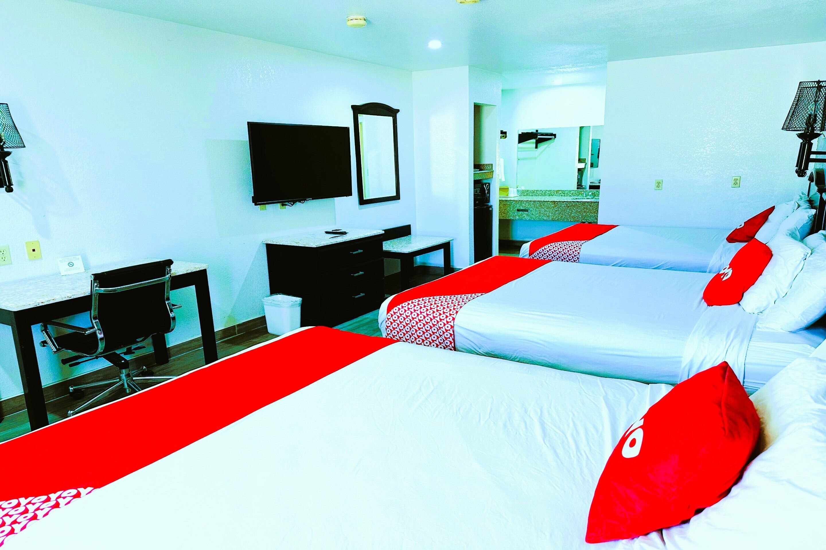 A hotel room with two beds, a desk, a chair, a TV, and a bathroom visible in the background.