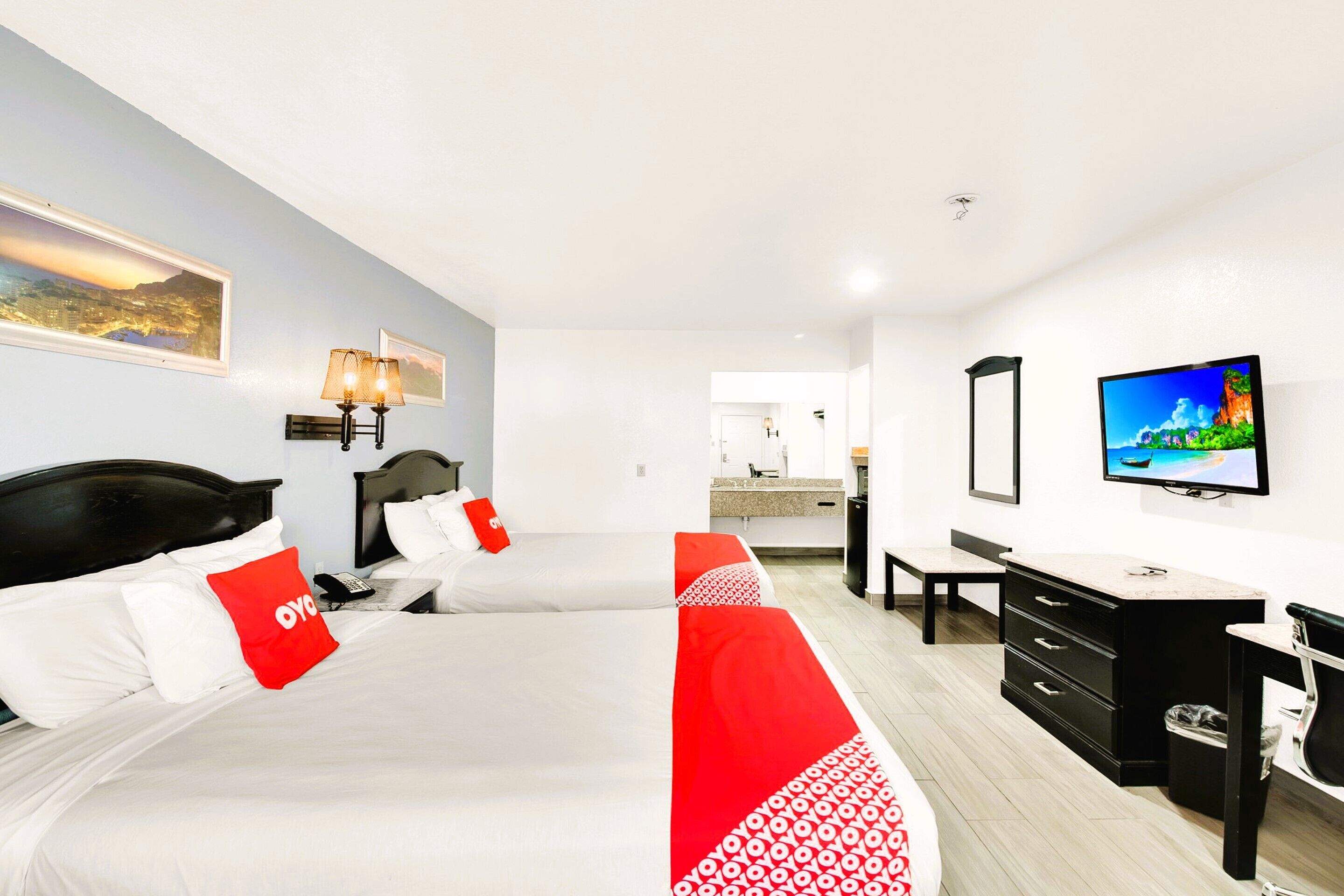 Habitación de hotel con dos camas, un escritorio, un televisor y un baño visible al fondo.