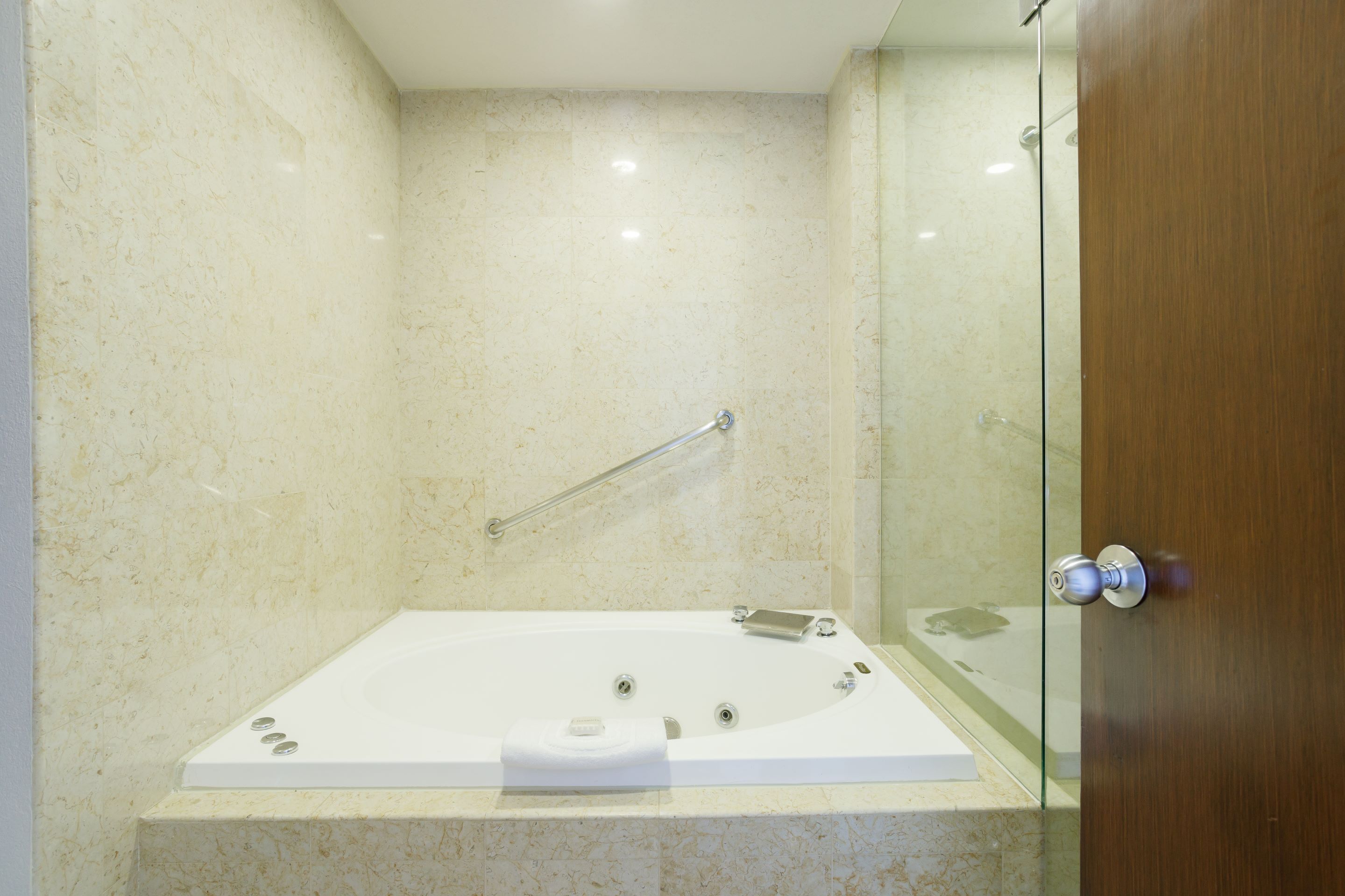 A modern bathroom with a glass shower enclosure, a white bathtub, and a wooden door.
