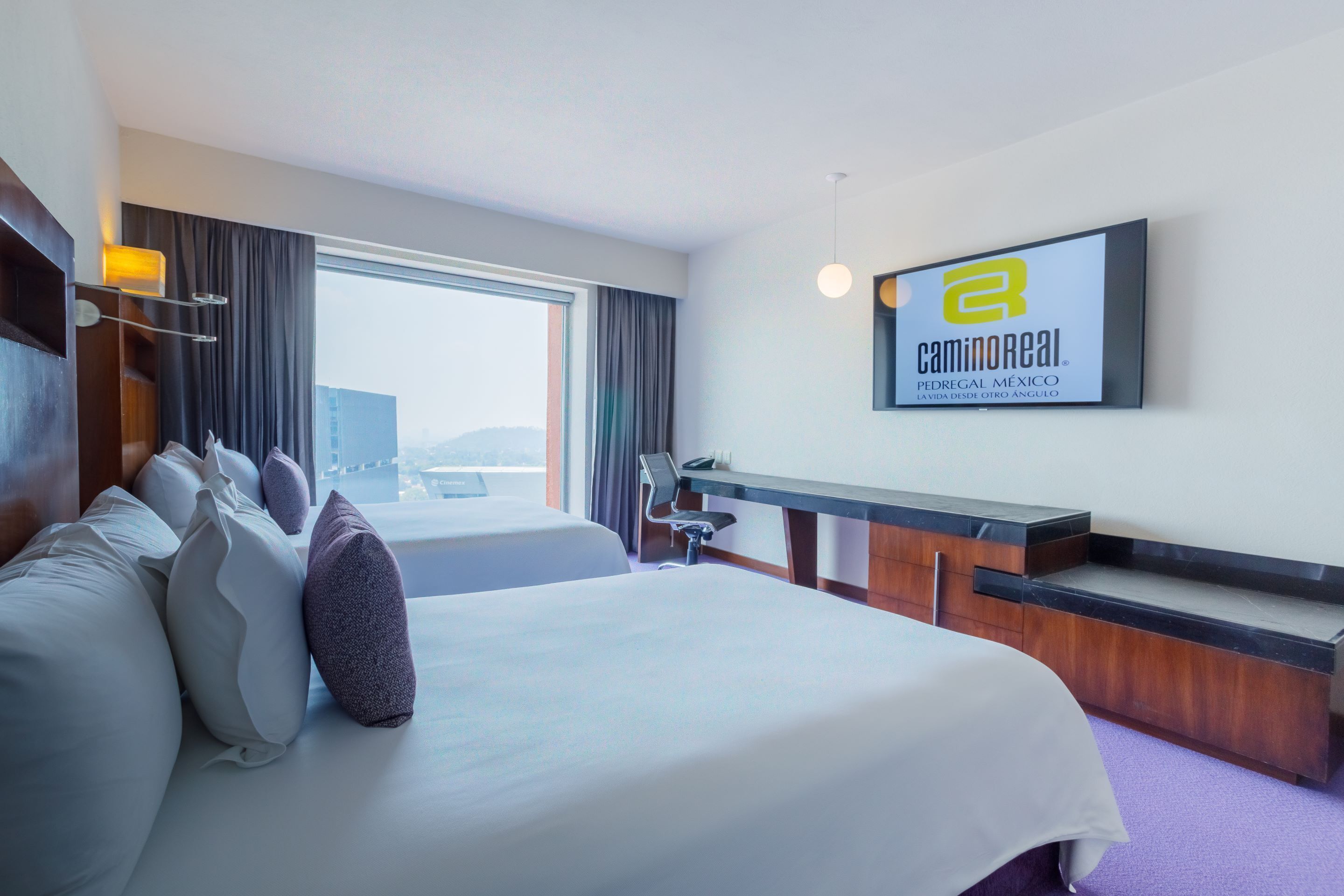 A hotel room with a large bed, a desk, and a TV on the wall.
