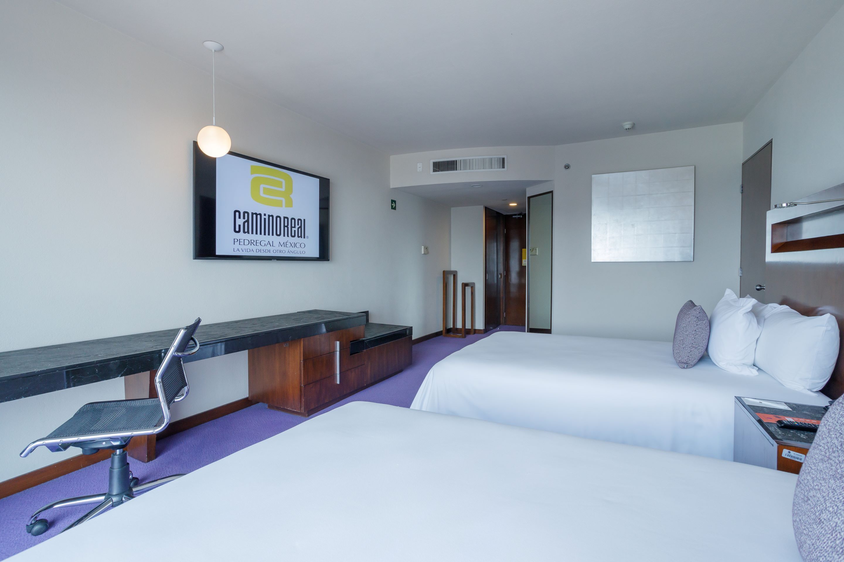 Une chambre d’hôtel avec deux lits, un bureau avec une chaise, une grande fenêtre et un panneau accroché au mur.