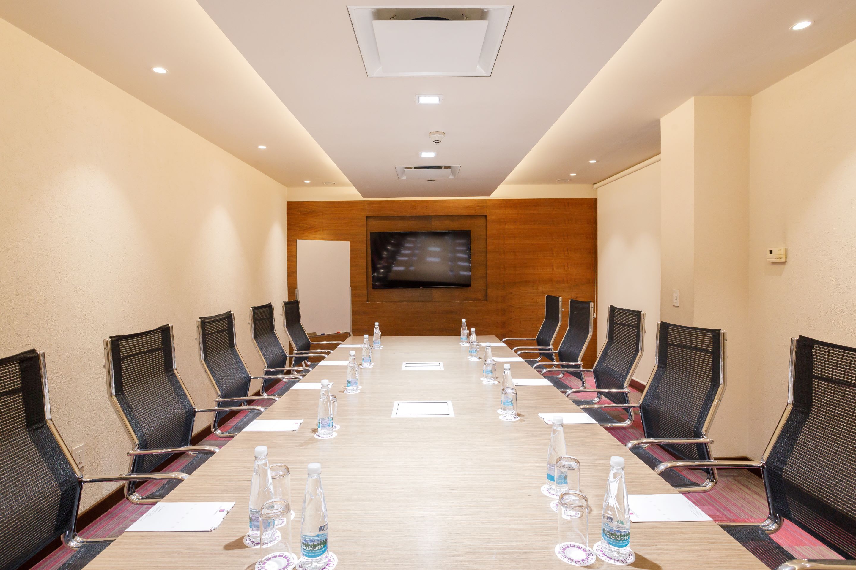 A conference room with a long table, chairs, and a television screen.