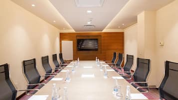 Un salón de conferencias con una mesa larga, sillas y una pantalla de televisión.