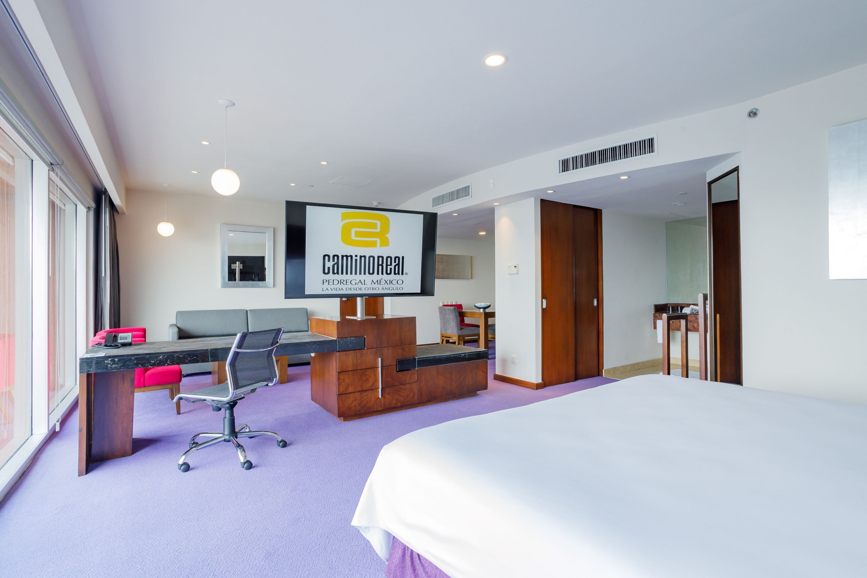 Habitación de hotel con cama, escritorio, computadora, silla y televisor.