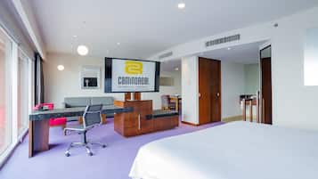 Habitación de hotel con cama, escritorio, computadora, silla y televisor.