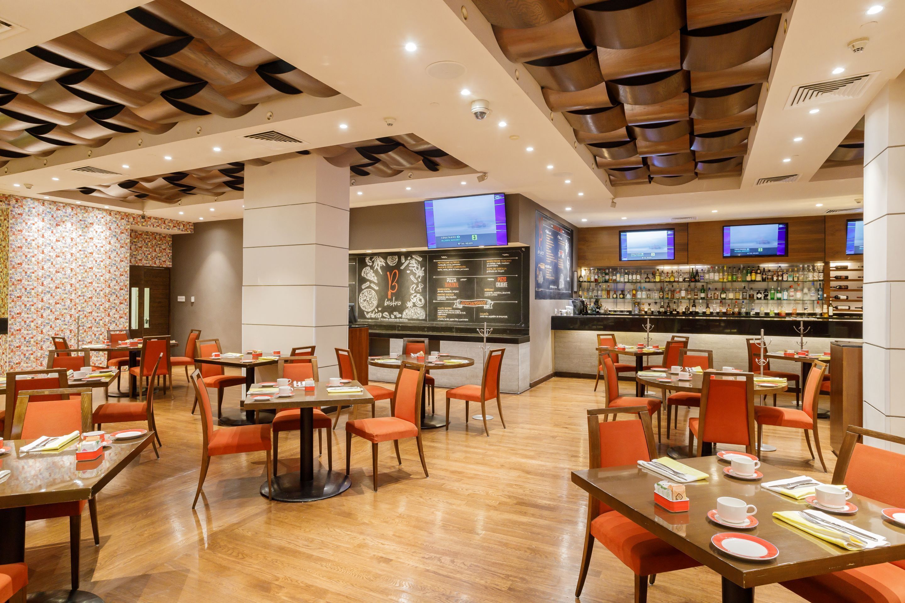 A restaurant with multiple tables and chairs, a bar area, and a menu board.