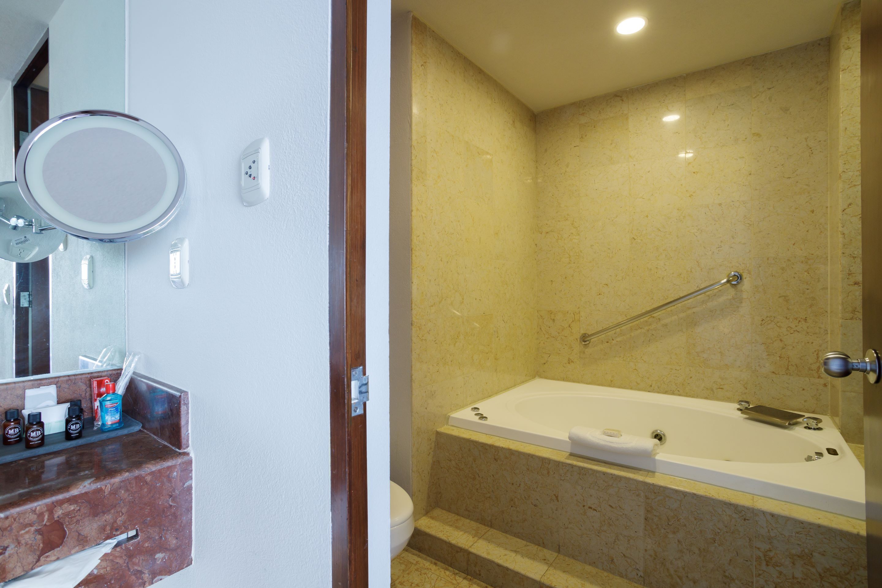 Une salle de bain avec un mur en marbre, une baignoire, des toilettes et un miroir.