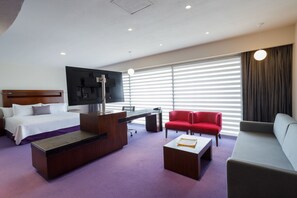 Une chambre d’hôtel moderne avec un lit, un bureau, une chaise rouge et un canapé.