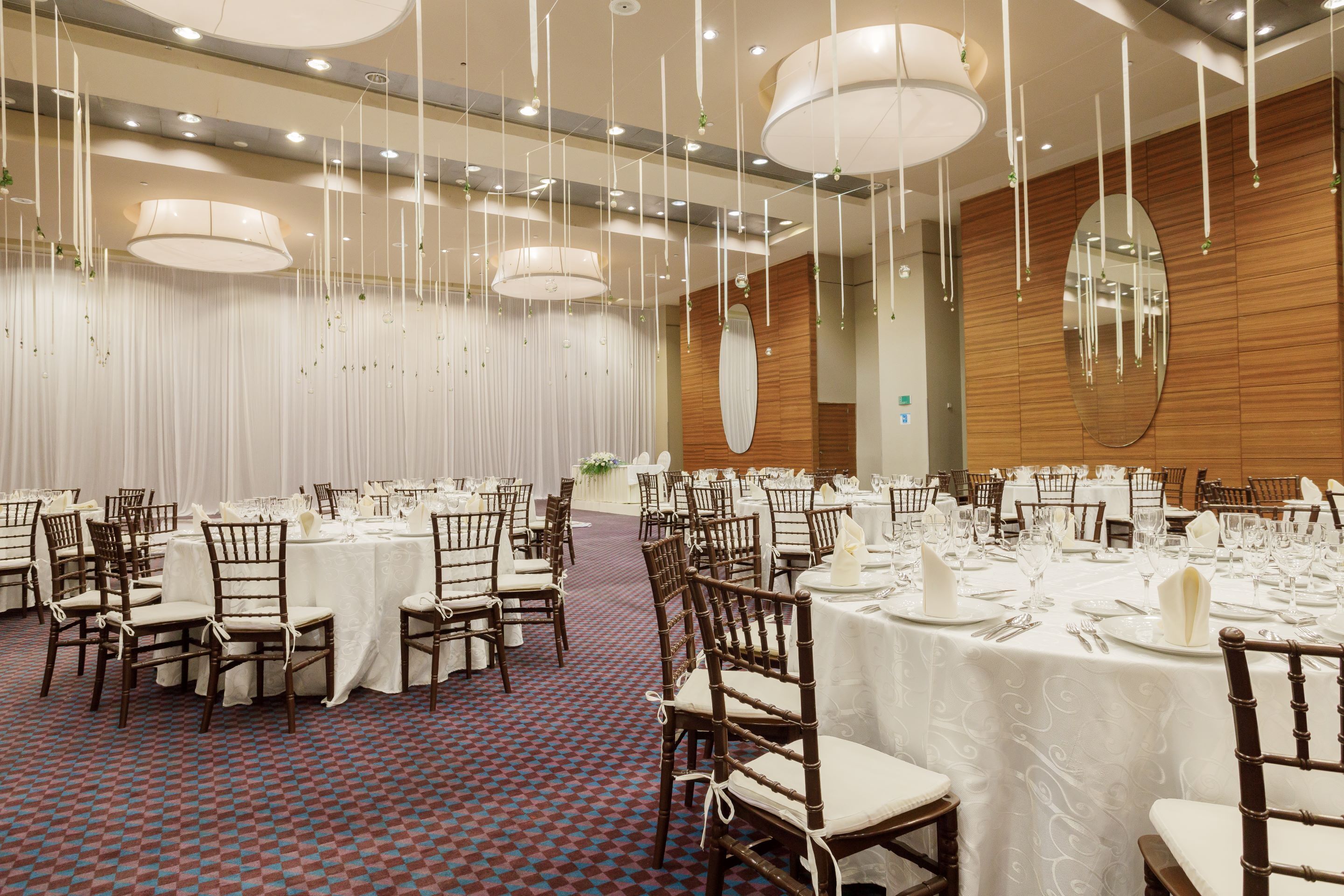 A banquet hall with round tables, chairs, and hanging light fixtures.