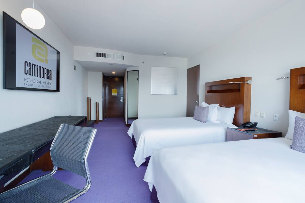 Ein Hotelzimmer mit zwei Betten, einem Schreibtisch, einem Stuhl und einem hölzernen Kopfteil.