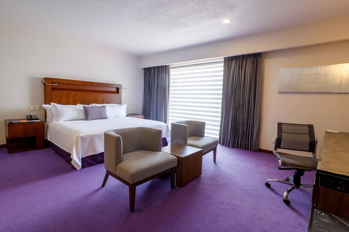 Ein Hotelzimmer mit einem Bett, zwei Sesseln, einem Schreibtisch und einem Stuhl.