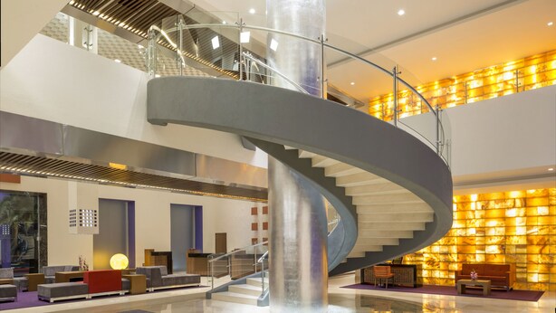 A modern lobby with a curved staircase, seating areas, and a reception desk.