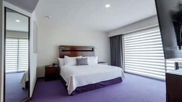 Ein Hotelzimmer mit einem großen Bett, einem Nachttisch, einem Fernseher und einem Fenster mit Jalousien.
