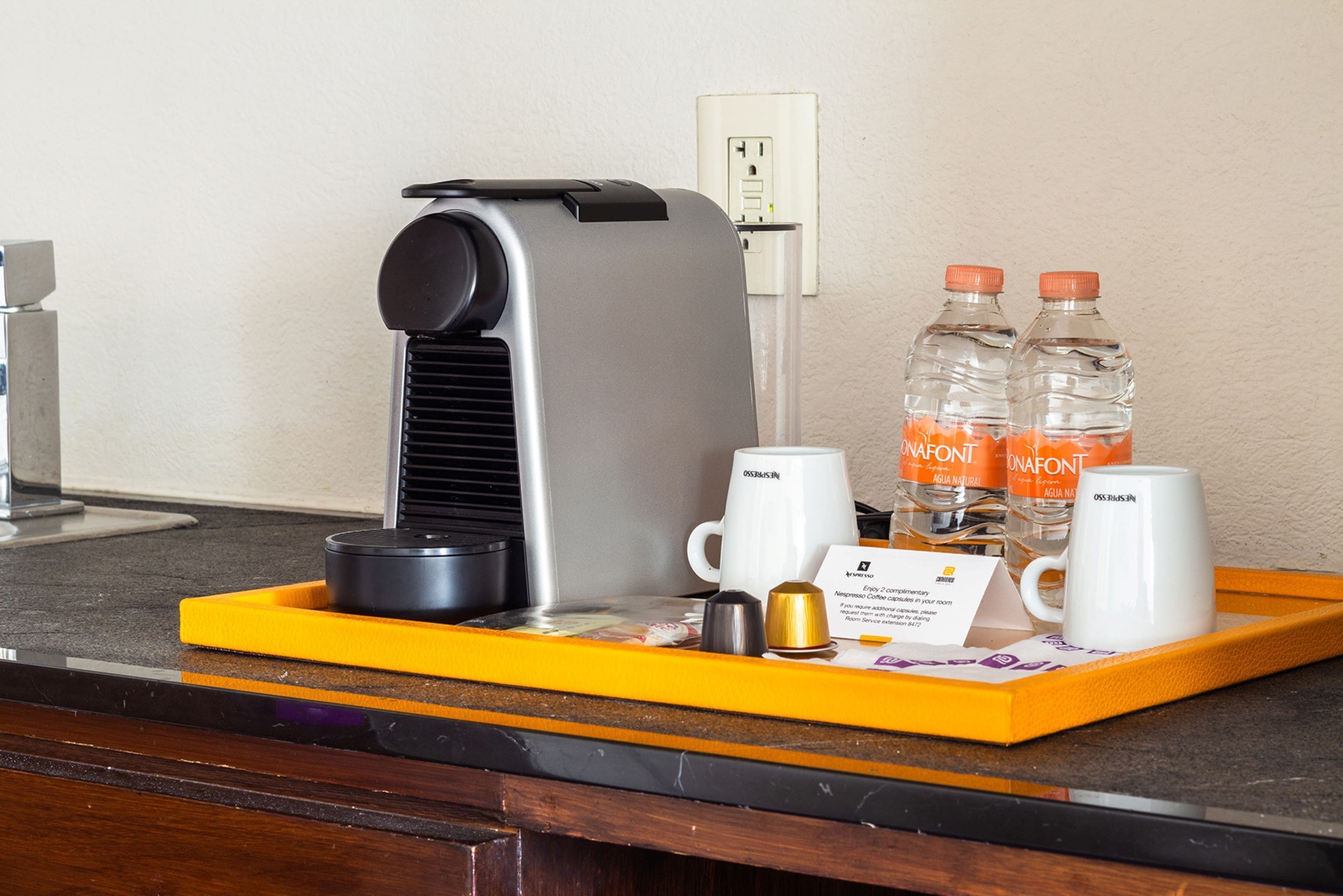 A coffee machine, two water bottles, two coffee cups, a tray, and a business card on a counter.