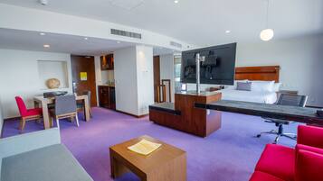 A hotel room with a bed, a desk, a TV, and a dining area.