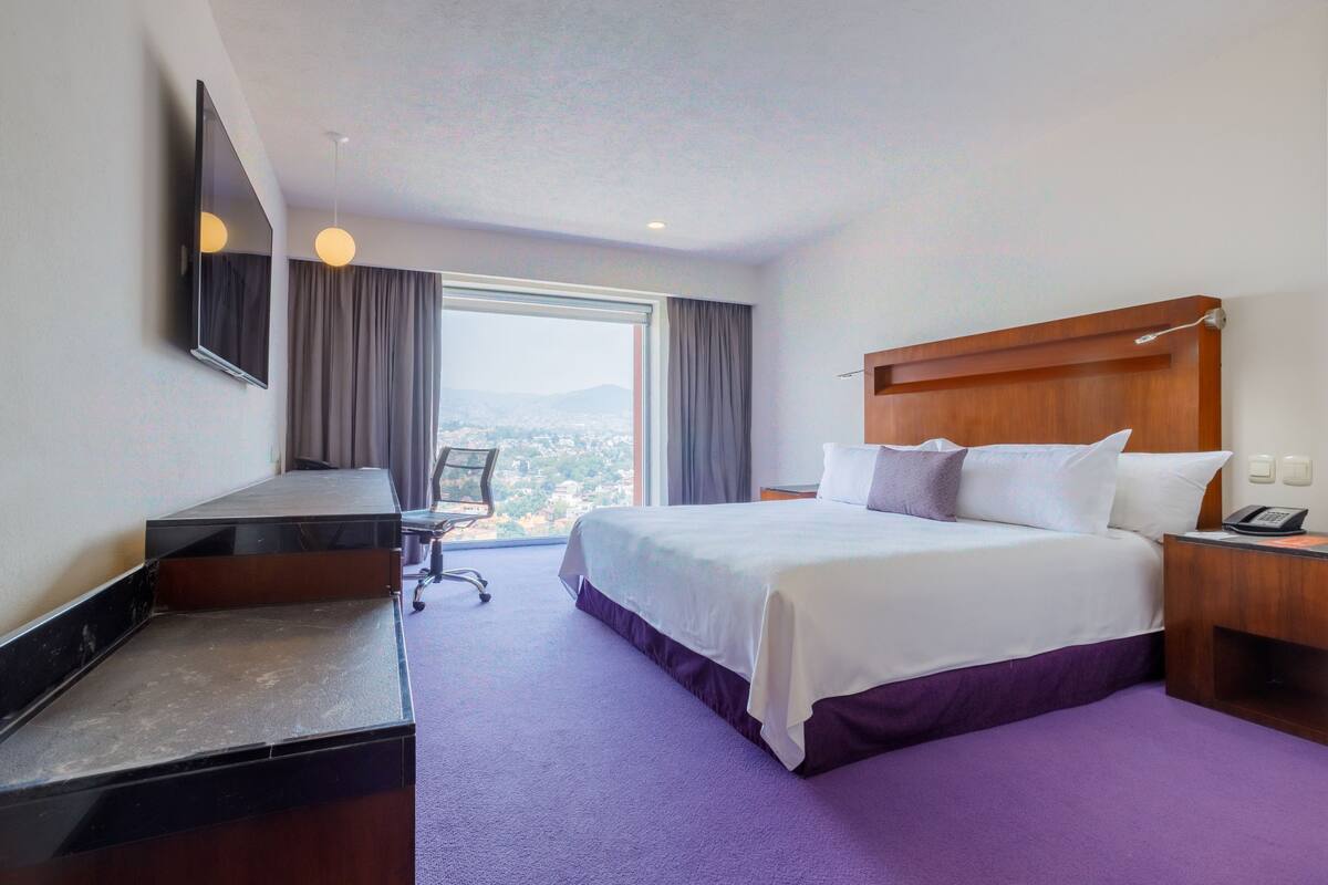 Ein Hotelzimmer mit Bett, Schreibtisch, Stuhl, Fernseher und Fenster mit Aussicht.