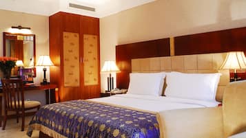 A hotel room with a large bed, two bedside tables, a desk with a chair, and a wardrobe.