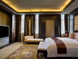 Una habitación de hotel con una cama grande, un televisor, un sofá, un pilar decorativo y una alfombra estampada.
